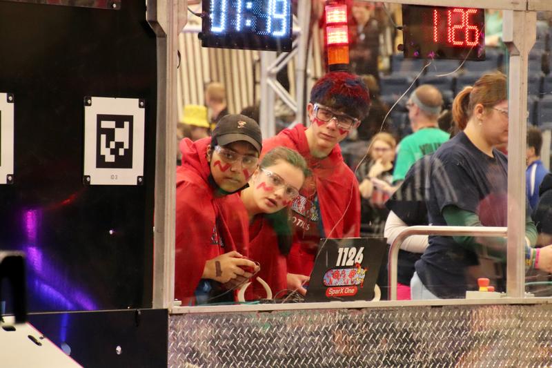 Three high school students looking at a robot.