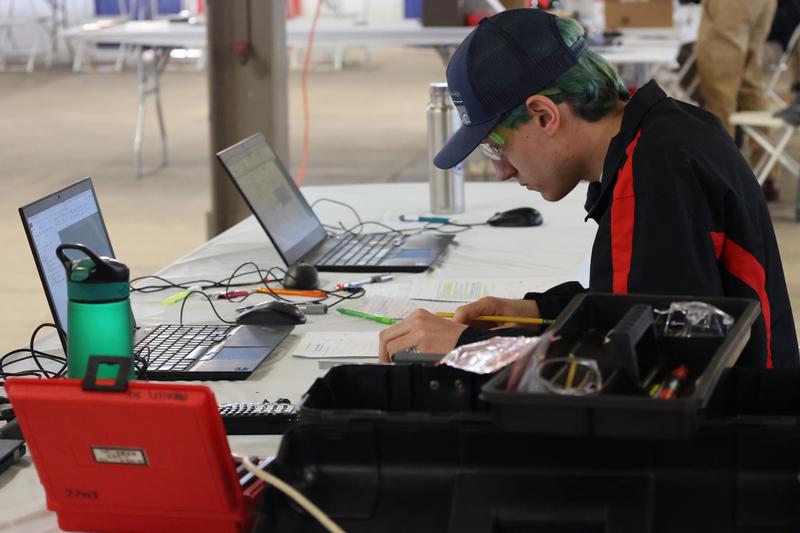 A teen boy workign with wires and a laptop.