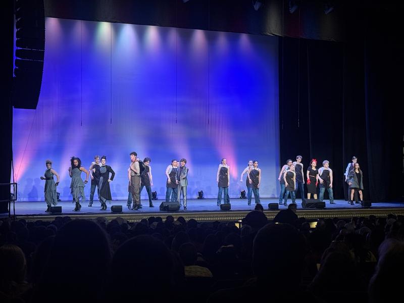 A group of teens dressed and gray and black clothing performing on a stage.