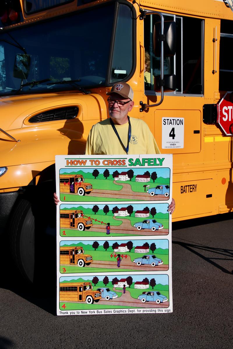 School bus driver holding a sign that reads School Bus Safety.