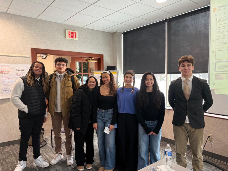 Seven smiling teens standing in a row.