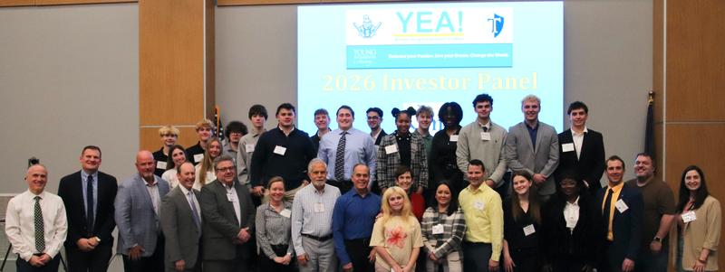 A large group of teens and adults gathered under a sign that read 'YEA!'.