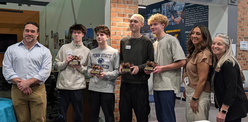Photo of four teens holding trophies and flanked by a man to the left and two women to the right.