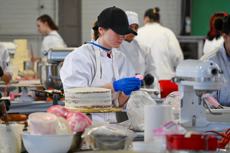 Teen decorating a cake with a frosting rose.