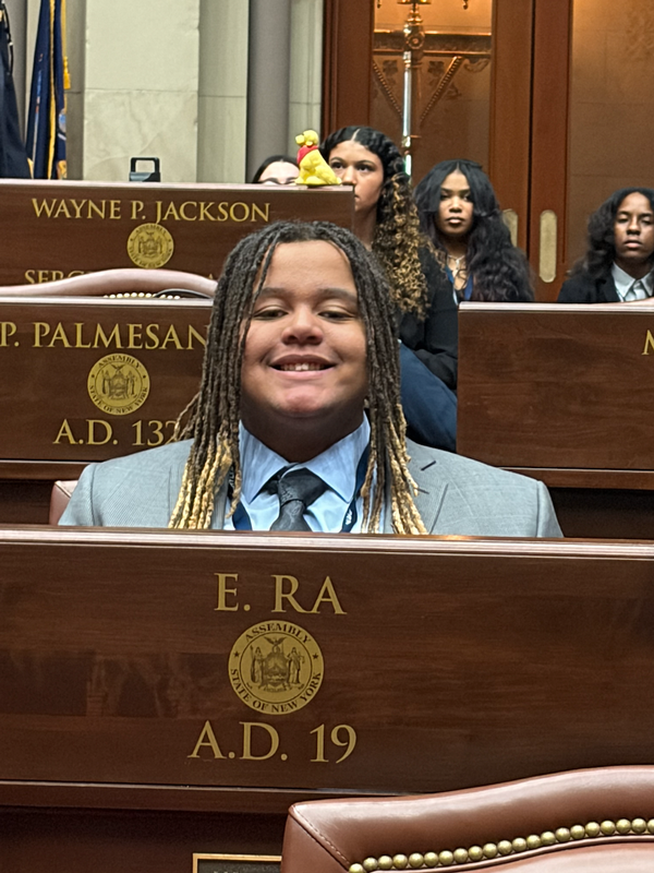 A teen in a suit seated in an assembly seat.