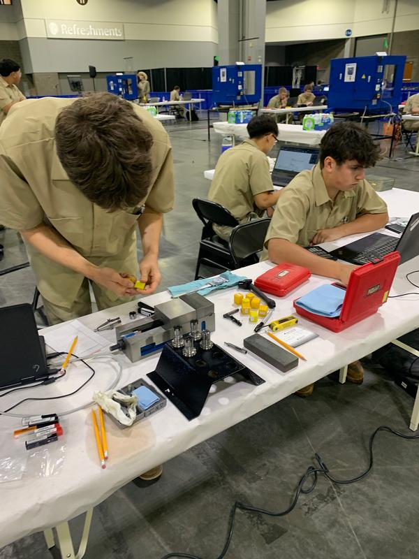 Three teens at a table with tools, wires and laptops in front of them.