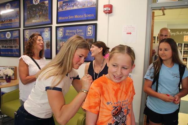 Young woman signing her autograph on the back of a student's shirt as the girl smiles.