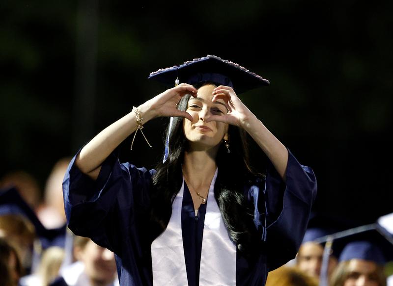 Teen in cap and gown makes a heart with her fingers