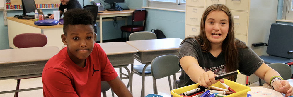 Two adolescants sitting at desks.