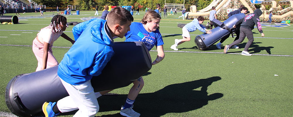 two teams of adolescents dragging tackling dummies.