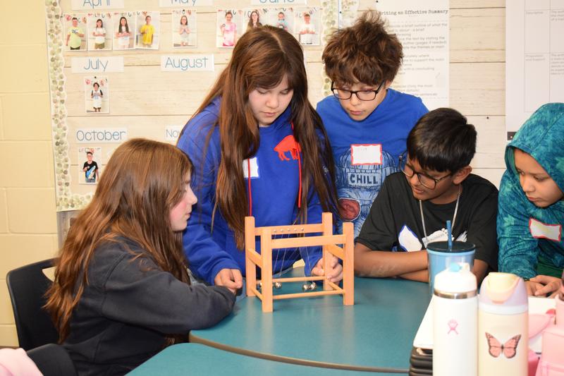 Four adolescents watching steel balls bounce off each other.